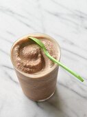 A banana and chocolate smoothie made with soy milk in a glass with a spoon