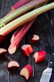 Rhubarb stalks on a wooden surface, some partially sliced