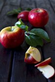 Apples with leaves, whole and chopped, on a wooden surface