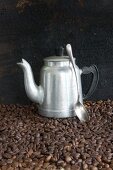 An aluminium coffee jug and a spoon on coffee beans