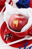 Apfel mit ausgestochenem Buchstaben in roter Tasse