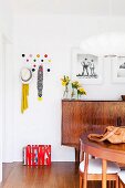 Wooden fifties sideboard, classic Hang-It-All coat rack next to black and white photos on wall and dining set in foreground