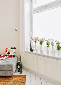 Flowers in collection of white vases on windowsill; partially visible sofa with scatter cushions to one side