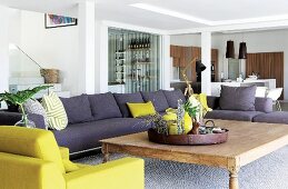 Sofa combination in grey and lime green with large wooden table in open-plan interior with staircase, bar and kitchen in background
