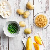 An arrangement of peas, potatoes, rice, beans, banana and orange (good carbohydrates)