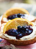 A wholemeal roll with blueberry and orange marmalade garnished with orange wedges