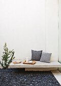 Scatter cushions, tea tray and stationary on minimalist bench made from stone slab in courtyard with dark gravel floor