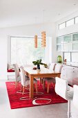 Holztisch und gepolsterte Stühle mit weißem Bezug auf rotem, gemustertem Teppich in modernem Esszimmer