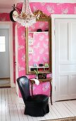 Schwarzer, lederbezogener Salonsessel vor Konsolentisch und gerahmter Spiegel an tapezierter Wand mit Schmetterlingmotiven auf rosafarbenen Hintergrund