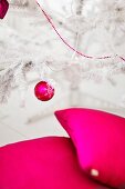 Cushions, Christmas bauble and string of beads in bright magenta on and around white, artificial Christmas tree