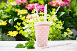 Three pink spotted paper cups and matching straws on a garden table