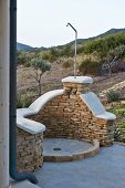 Outdoor shower with half-height stone wall in front of Mediterranean landscape