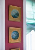 Vertical row of framed landscapes in gilt mounts on claret wall