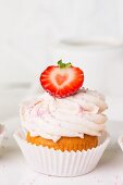 A strawberry cupcake decorated with pink sugar pearls