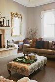 Tea set on tray on ottoman and timeless sofa in front of fireplace; gilt-framed mirror on background