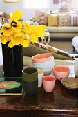 Yellow calla lilies in black vase and stacked beakers and bowls on battered table top