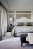 Double bed with curved, white-painted wooden headboard against wood-panelled wall with white frames in elegant bedroom
