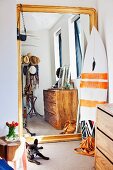 Full-length gilt-framed mirror leaned against wall next to surfboard in niche