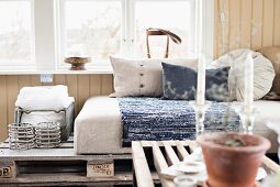 View across coffee table to couch made from wooden pallets and pale cushions below window