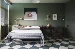 Vintage bed with grey metal frame below modern artwork on wall painted olive green in bedroom with chequered floor