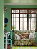 Comfortable sofa with vintage floral pattern below wooden lattice window and rug with bright green stripes in living area with green walls