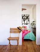 Schlichter Klappstuhl aus Bambus im Vorraum an Wand, seitlich offene Tür und Blick auf Bett mit Palmenmotiv an Wand