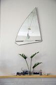 Mirror in shape of sailing boat above arrangement on mantelpiece