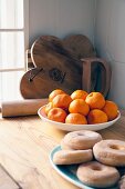 Tangerines and ring doughnuts on kitchen worksurface; wooden boards and rolling pin in background