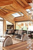 Open-plan interior with leather sofa in modern chalet with exposed wooden roof structure and glass walls