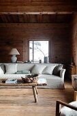 Helles Hussen-Sofa mit Kissen, davor rustikaler Holz Couchtisch im Wohnzimmer einer Hütte