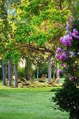 Seating area in large, summery garden with sun loungers between pillars