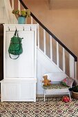 White-painted, wooden cloakroom cabinet in front of staircase in rustic hallway with patterned tiled floor