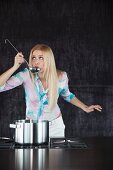 A woman tasting from a ladle held over a pot on a stove