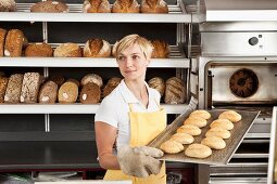 A woman holding a tray of freshly baked rolls in a bakery