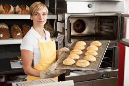 A woman holding a tray of freshly baked rolls in a bakery
