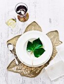 Leaf with hand-written name on white plate and fabric place mat shaped like a leaf arranged on white wooden table