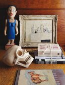 Stillleben mit Totenkopf und Bücherstapel vor bemalter Holzfigur neben Bild auf Tisch