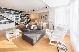 Weisser Schaukelstuhl neben moderner Sofakombination in Grau in offenem Wohnraum, im Hintergrund Essplatz