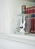 Raving Rabbid figurine under upturned preserving jar in front of books with high-quality bindings on shelf of old kitchen dresser