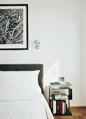 Retro-style side table next to bed with grey upholstered headboard and Tolomeo lamp on wall next to framed drawing