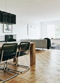 Cantilever chairs with black covers at modern wooden dining table; corner couch in background in minimalist interior