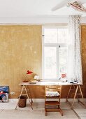 Tripp Trapp Kinderstuhl vor improvisiertem Arbeitstisch mit Holzböcken am Fenster, unrenovierte Wand