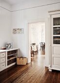 Traditional country-house kitchen with white-painted cupboards, view into dining room through open door and continuous wooden flooring