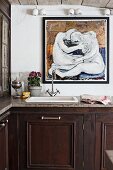 Kitchen counter with dark wooden base units, vintage tap fittings above sink and modern painting on wall