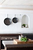 Kitchen utensils on counter and cast iron pans on wall next to arched niche