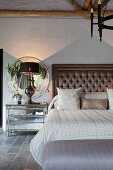 Double bed with button-tufted headboard and table lamp on bedside table below round mirror in elegant vintage bedroom