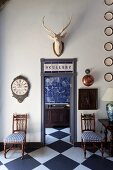 Antique chairs with blue and white seat cushions flanking open door with view of kitchen counter and blue-tiled wall in vintage interior