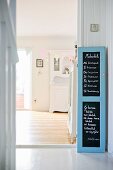 Writing on blackboard in pale blue, cupboard door frame next to doorway leading to dining room with view of white, old-fashioned dresser