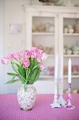 Rosa Tulpenstrauss in Vase und Kerzenhalter mit weissen Kerzen auf rosa-weiss gemusterter Tischdecke