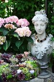 Pink hydrangea next to bust of woman and large wreath of succulents